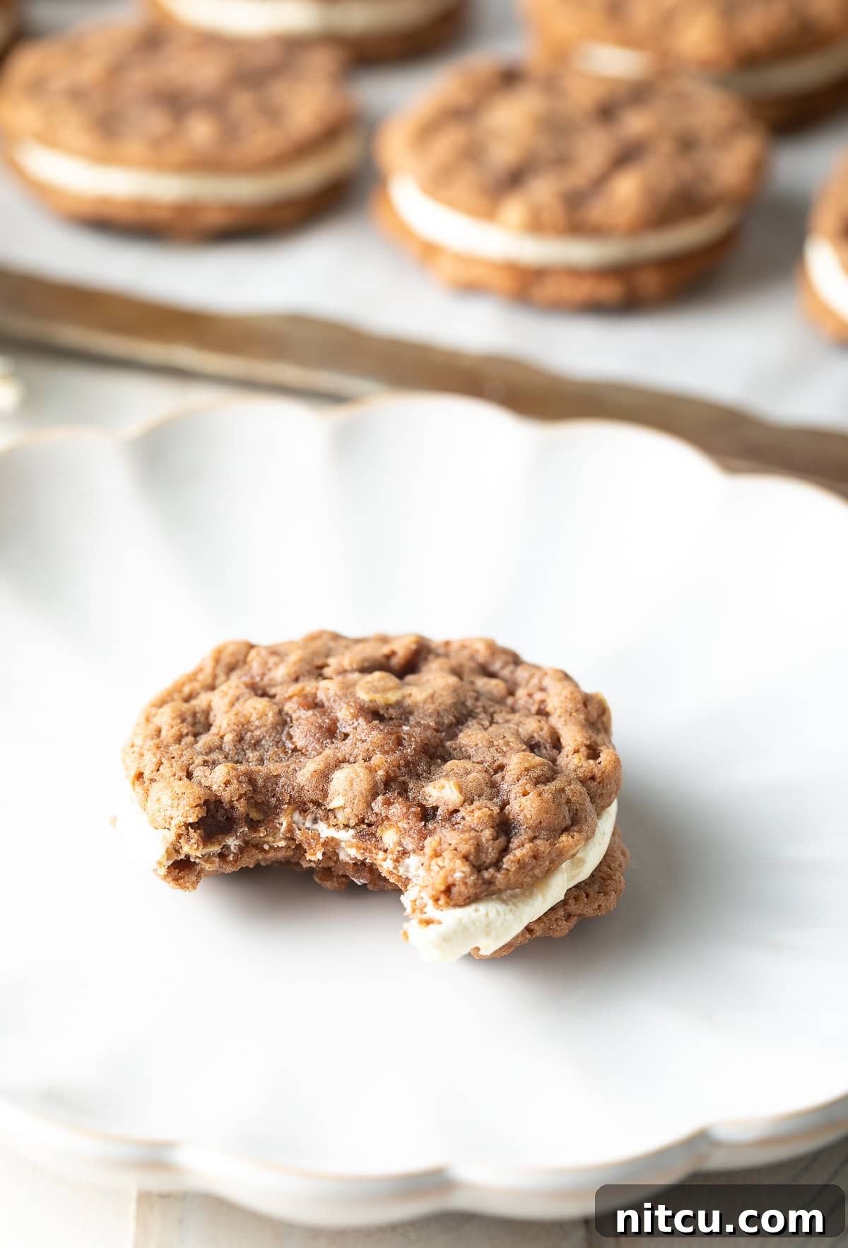A delectable homemade oatmeal cream pie on a plate with a bite taken out, revealing its fluffy cream filling.