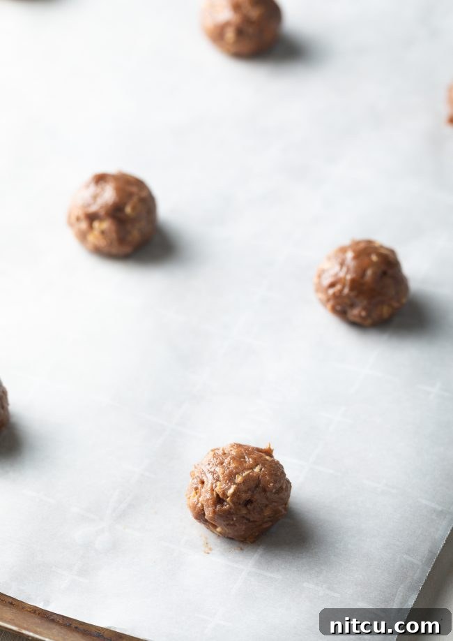 Balls of oatmeal cookie dough perfectly portioned on parchment paper-lined baking sheets.