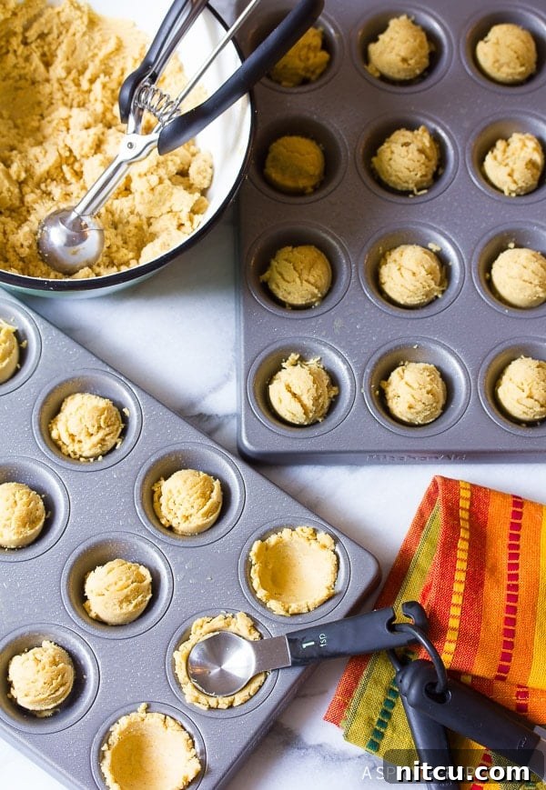 Masa batter being carefully spooned into individual compartments of a mini muffin tin.