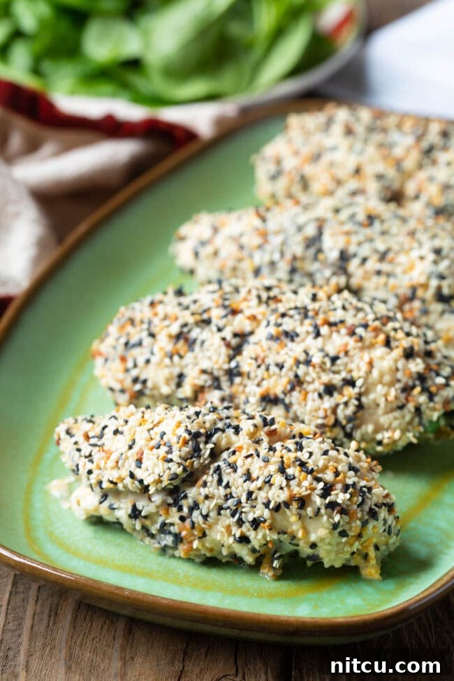 Five perfectly rolled chicken breasts, generously coated in everything bagel seasoning, resting elegantly on a vibrant green plate, showcasing their golden, crispy exterior.