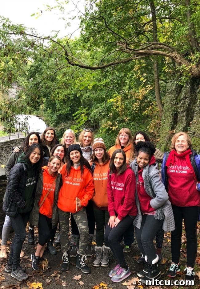 A group of fourteen diverse women, all wearing matching SkinnyTaste hoodies, posing together for a celebratory group photo.