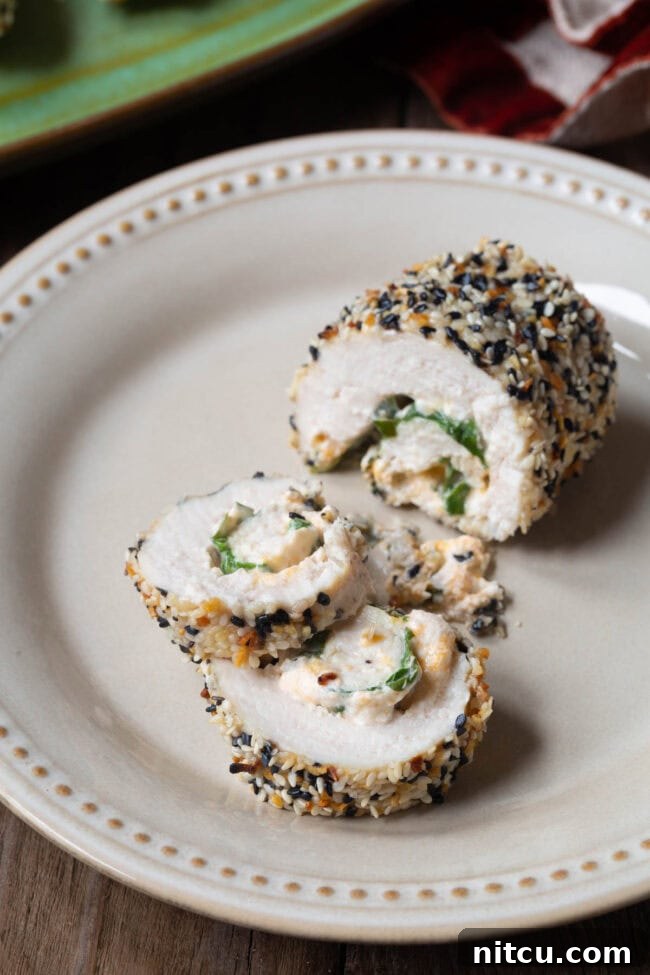 A perfectly cooked chicken breast roll, sliced into three distinct pieces, revealing the creamy blend of cream cheese, spinach, and cheddar cheese filling nestled inside its golden, everything bagel-seasoned crust.