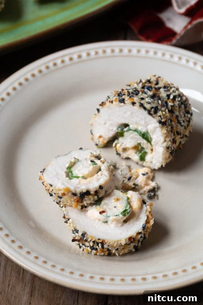 A perfectly cooked chicken breast roll, sliced into three distinct pieces, revealing the creamy blend of cream cheese, spinach, and cheddar cheese filling nestled inside its golden, everything bagel-seasoned crust.