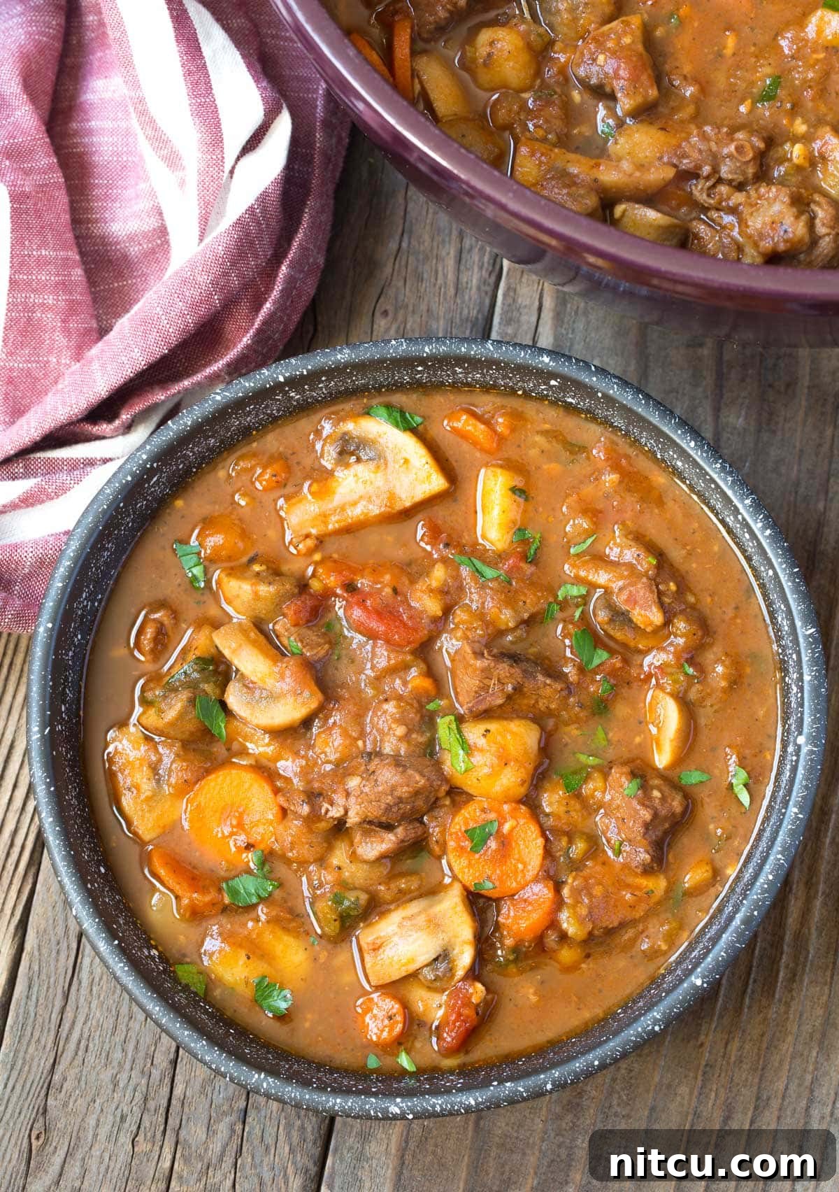 A comforting bowl of easy beef stew, with more stew simmering in a pot in the background. Best comfort food.