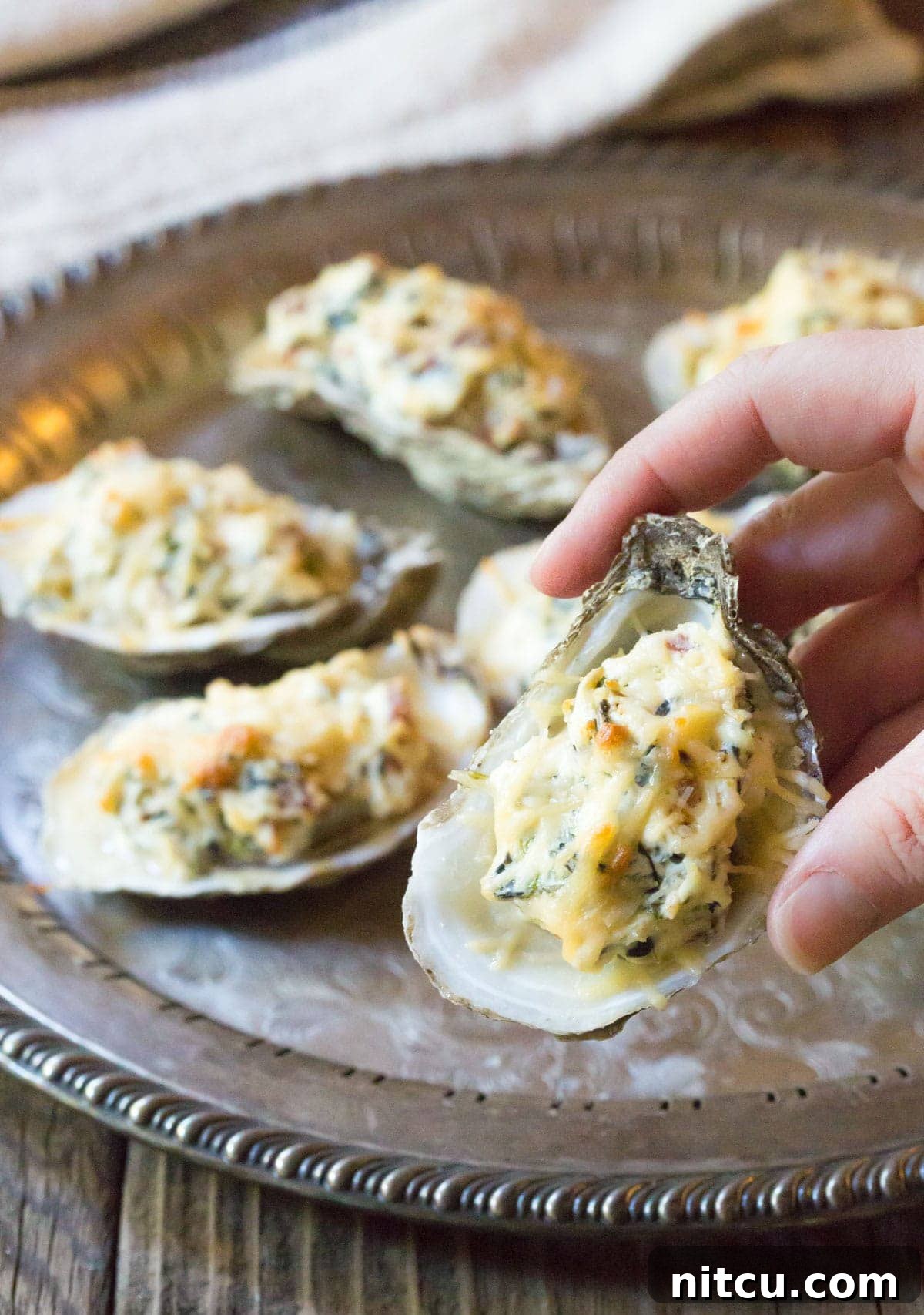 Close-up of a cheesy baked oyster in hand, ready to be enjoyed