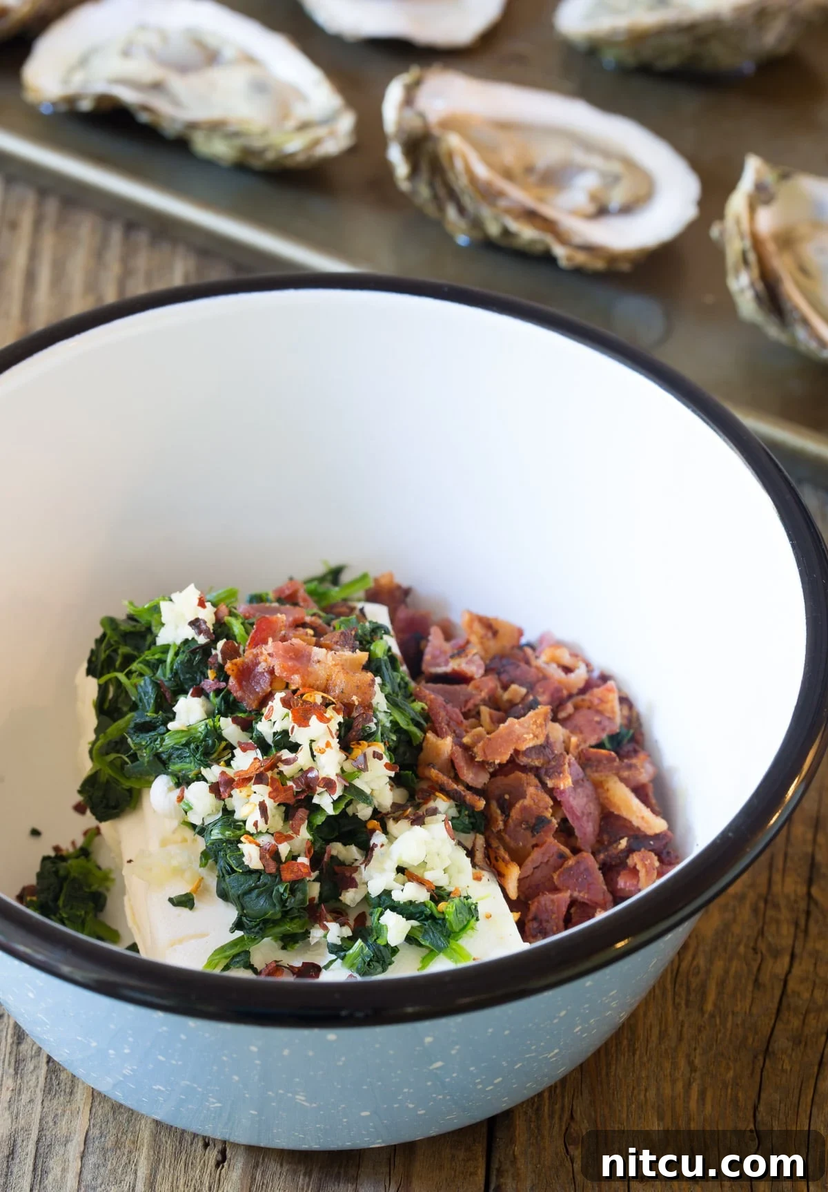 Close-up of cooked oysters featuring the melted three-cheese filling and crumbled bacon
