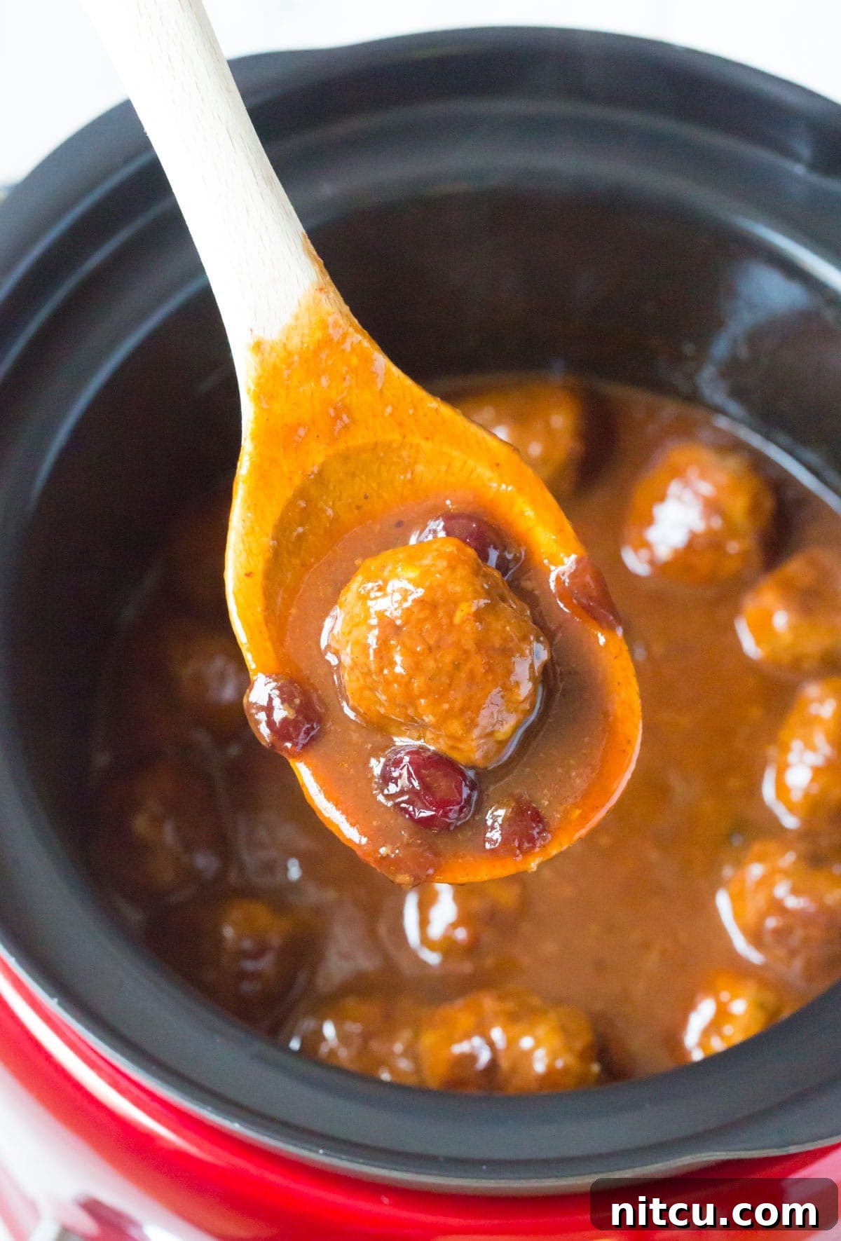 Close-up of a single cocktail meatball on a wooden spoon, coated in rich cranberry BBQ sauce