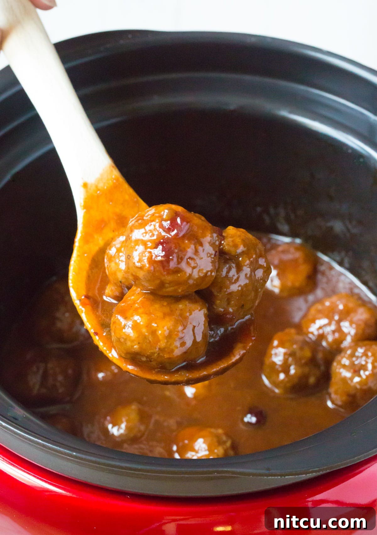 Final presentation of slow cooker cocktail meatballs in sauce on a wooden spoon