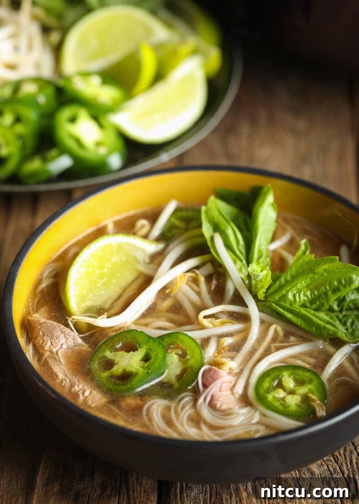 Close-up shot of rich pho broth with translucent low-carb noodles in a black bowl, ready for garnishes.