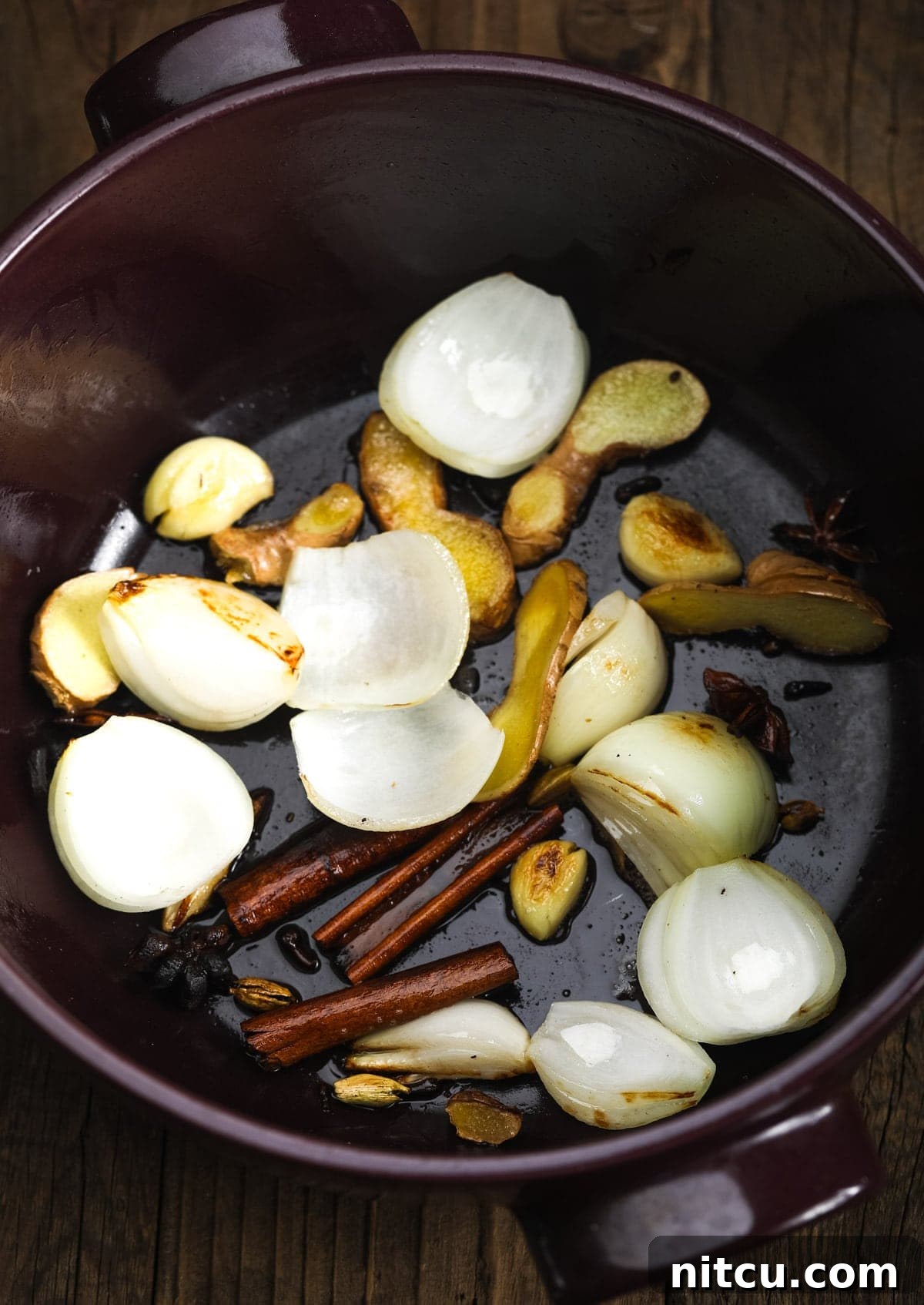 Onion, ginger, garlic, and whole spices sizzling in coconut oil at the bottom of a large pot, beginning to release their rich aromas.