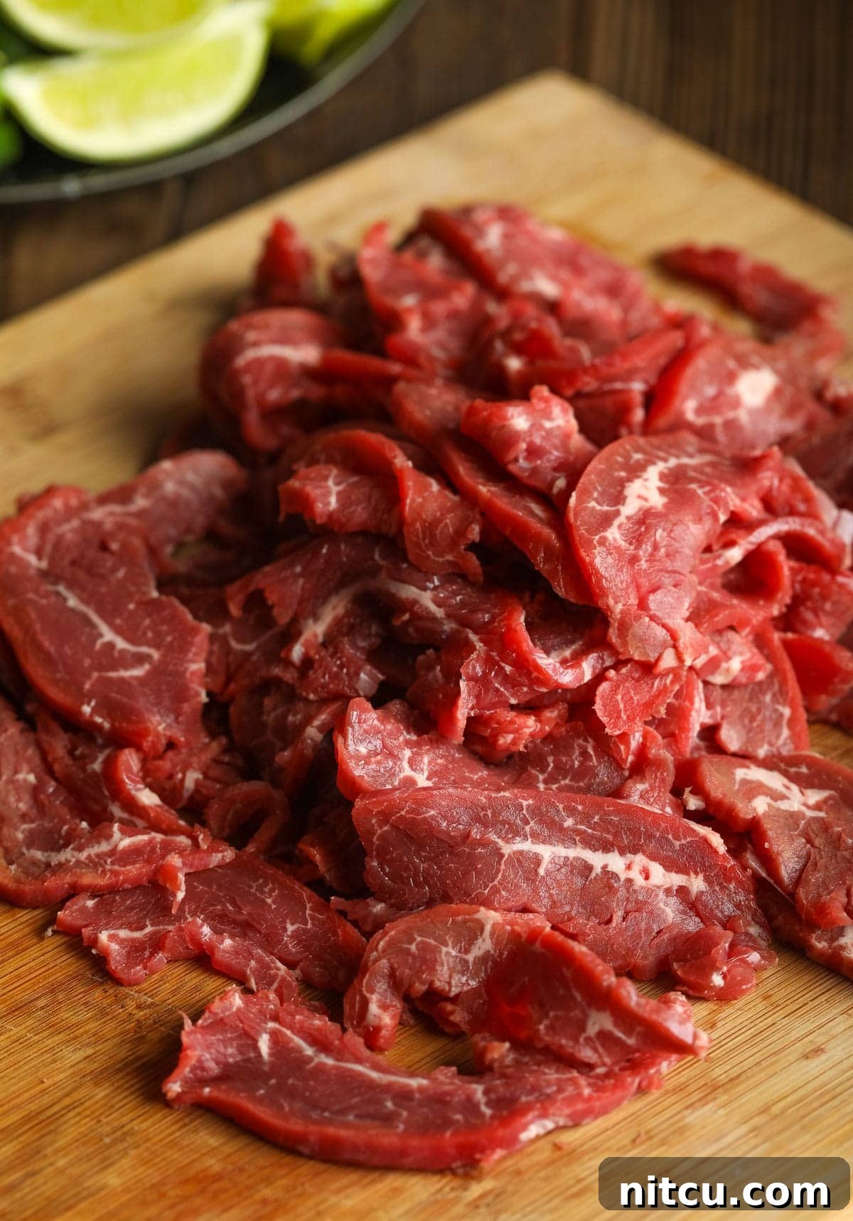 Raw flank steak, expertly thinly sliced against the grain on a rustic wooden cutting board, ready for the pho.