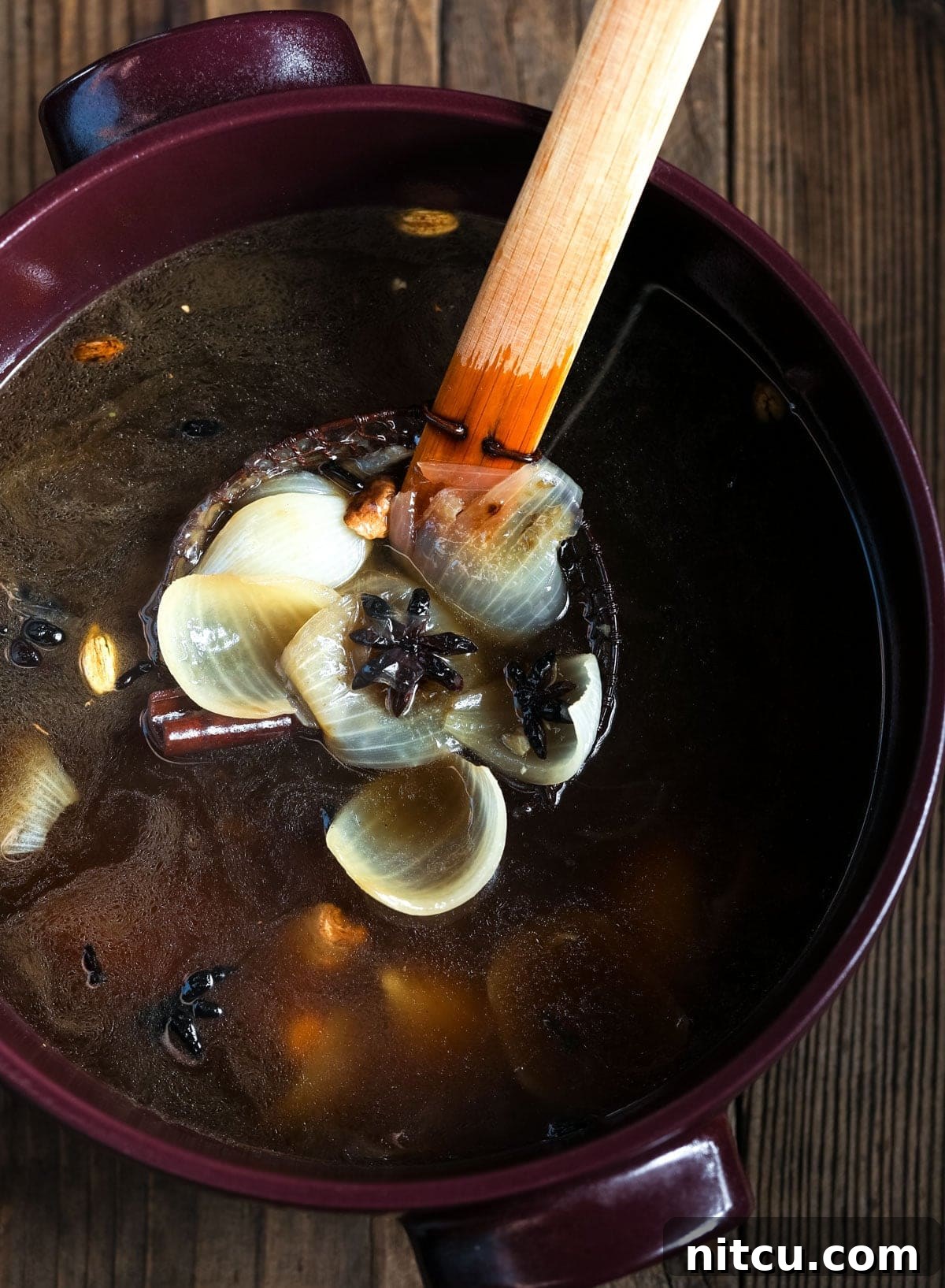 A ladle gently skimming aromatics from a large pot of rich Vietnamese broth, leaving a clear and flavorful base.