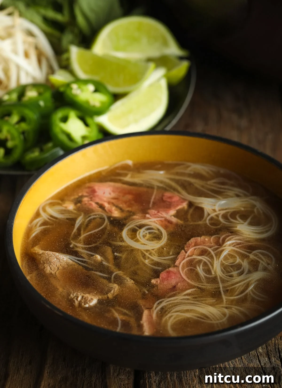 A steaming bowl of healthy paleo pho soup, featuring low-carb noodles and thinly sliced beef, with a rich broth.