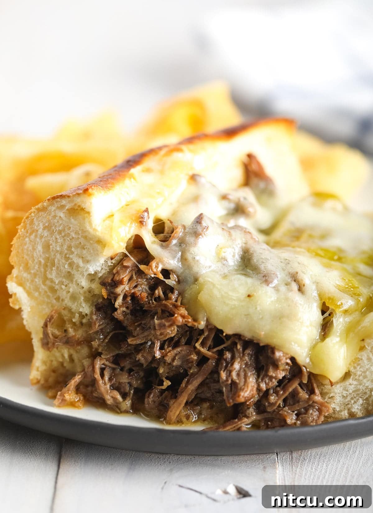 Shredded Instant Pot Italian beef sandwich with perfectly melted provolone cheese on top, served on a white plate with a side of au jus.