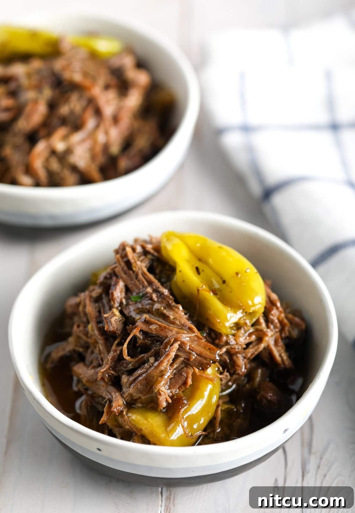 Two white bowls brimming with delicious Italian beef and vibrant green pepperoncini peppers, ready to be served.