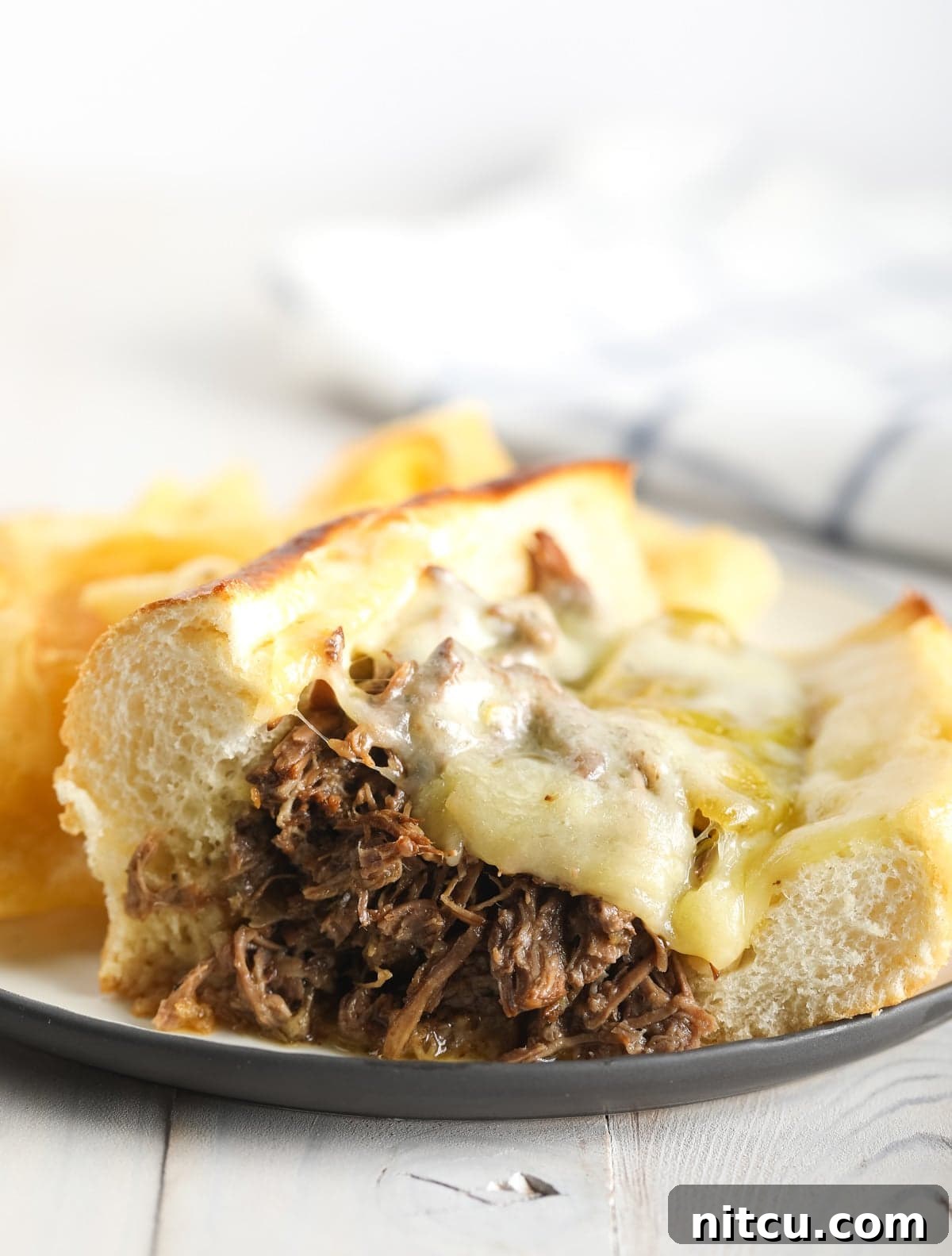 A perfectly prepared Italian beef sandwich with melted provolone cheese, served on a white plate with visible juices.