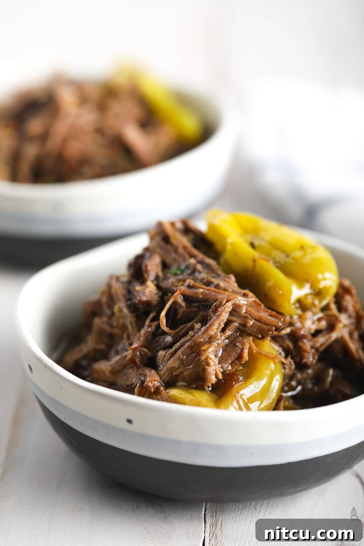 Close-up of Italian-style shredded beef in a bowl, generously garnished with bright green pepperoncinis.