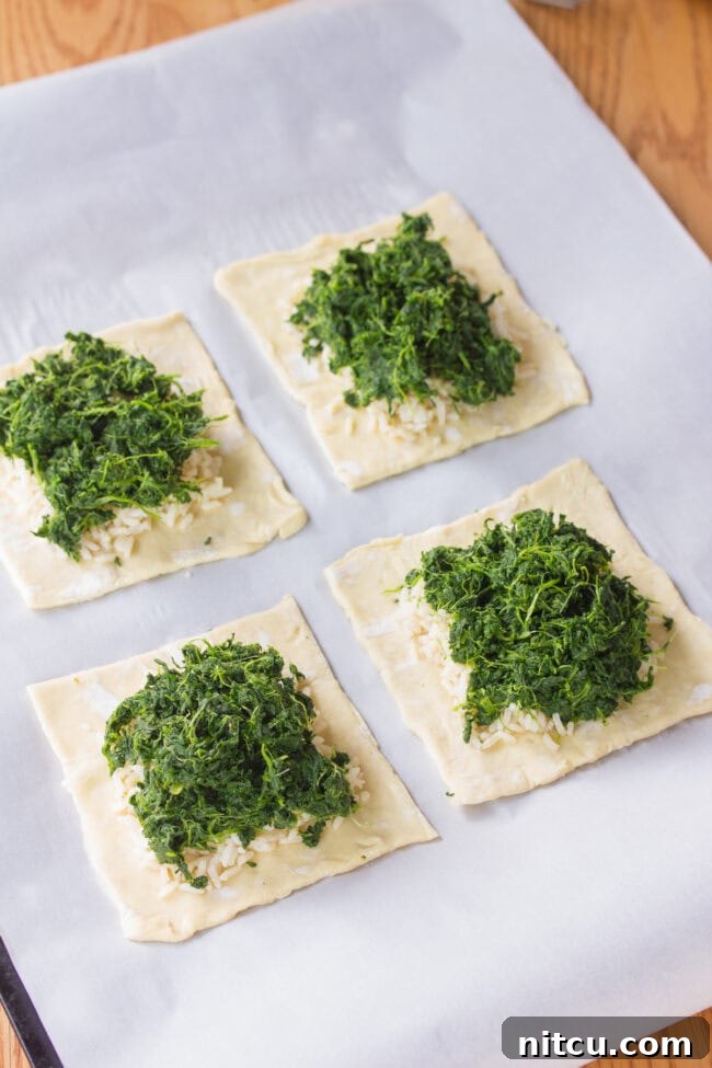 Puff pastry sheet with a vibrant layer of wilted spinach spread evenly, forming the base for the Salmon Coulibiac filling.