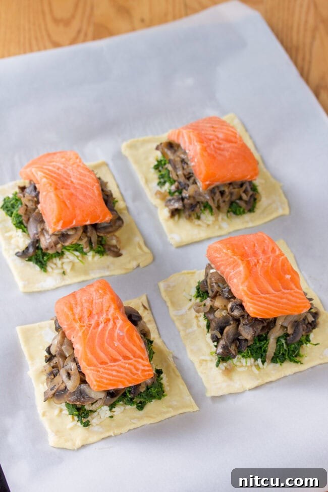The process of layering Salmon Coulibiac ingredients: puff pastry, rice, spinach, mushrooms, and salmon fillet arranged meticulously.