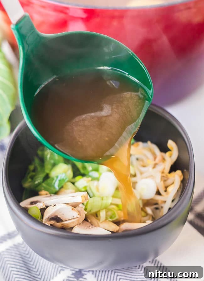 Ladle pouring broth over veggies in a bowl.