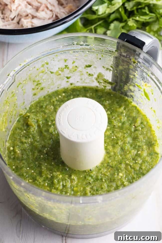 Tortillas being dipped in salsa verde in a shallow pan.