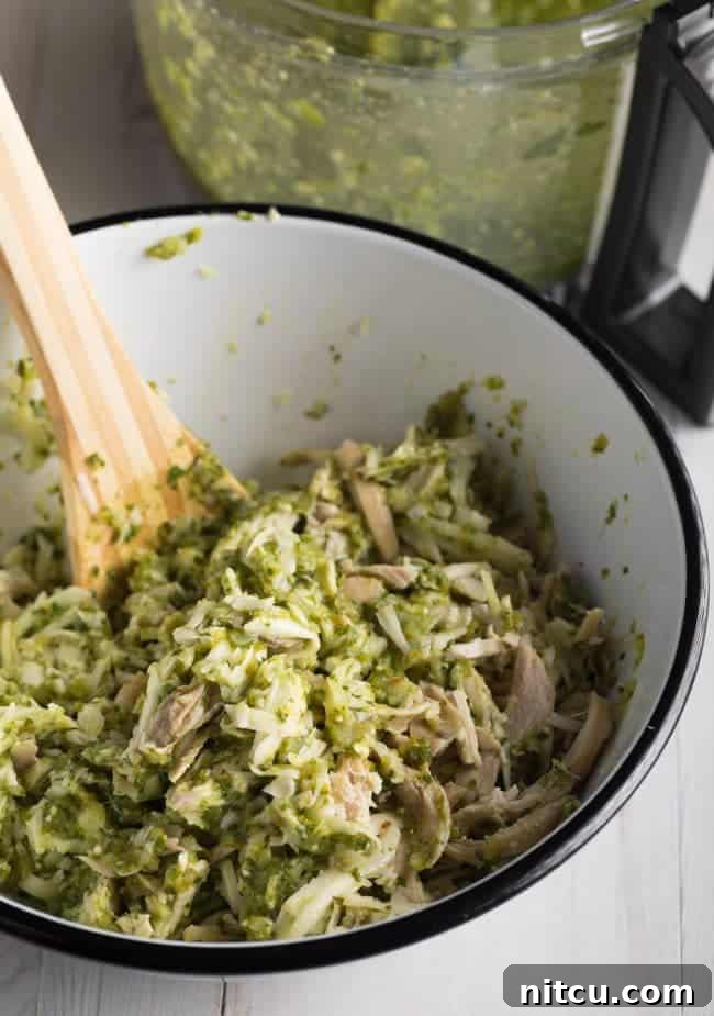 Shredded chicken being mixed with salsa verde sauce in a bowl.