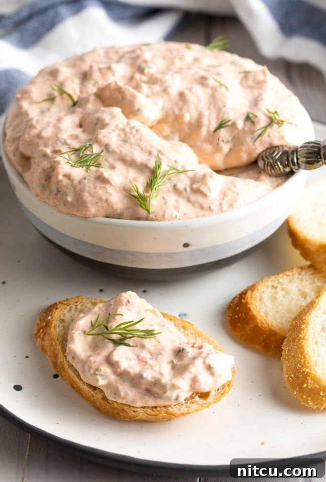 A small metal spreader knife delicately loaded with creamy smoked salmon dip, resting on a piece of toasted bread, showcasing perfect serving.
