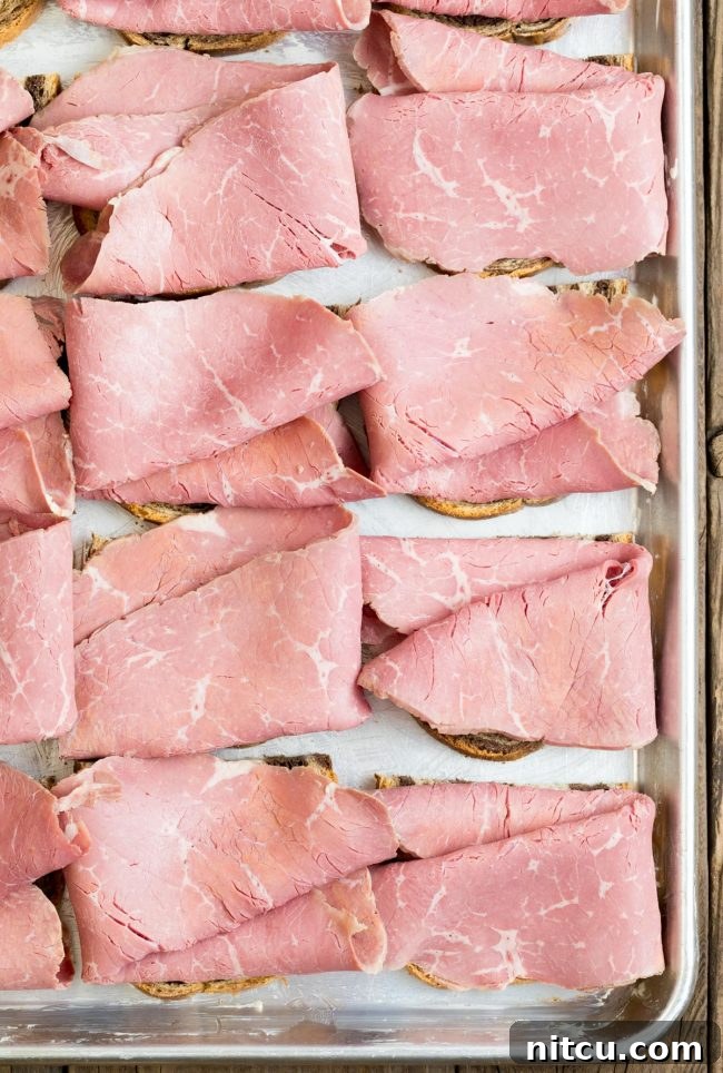 Rye bread assembled with generous slices of corned beef on a sheet pan, ready for the next layer.