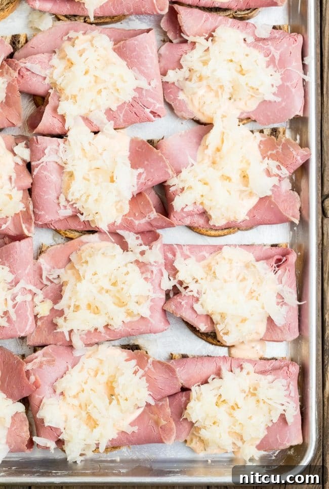 Rye bread topped with neatly arranged corned beef and a mound of sauerkraut on a sheet pan.
