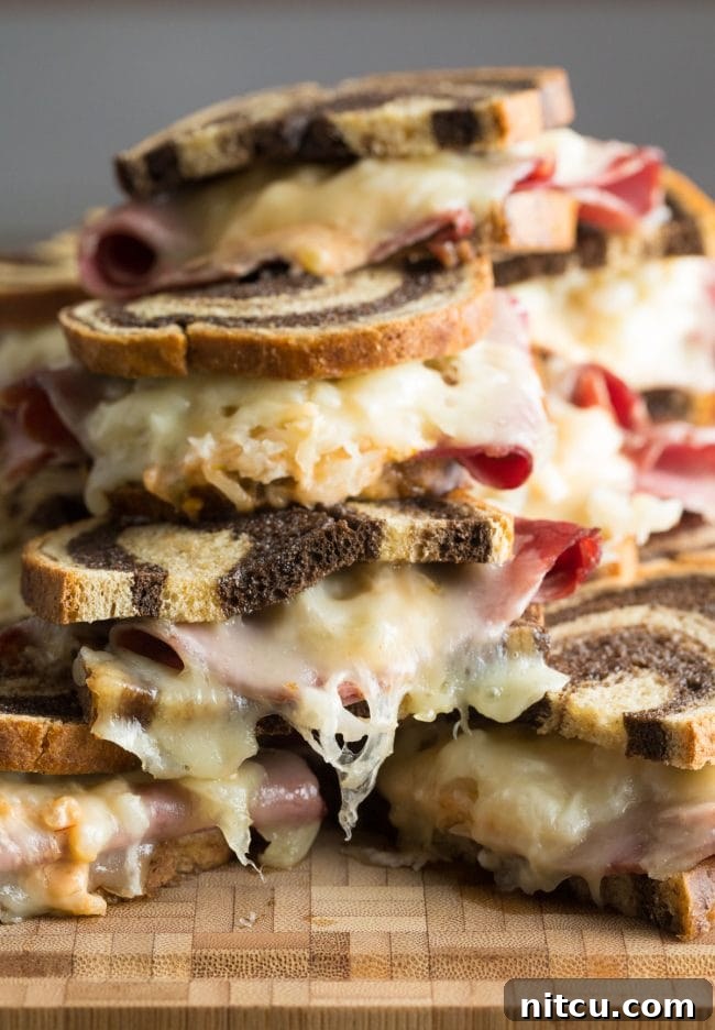Baked Reuben sandwiches generously piled on top of each other, ready to be enjoyed.