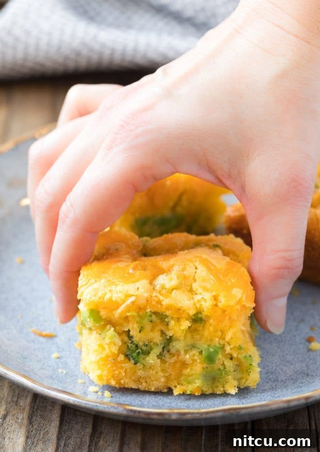 Hands reaching for a piece of Jiffy Broccoli Cornbread from a pan