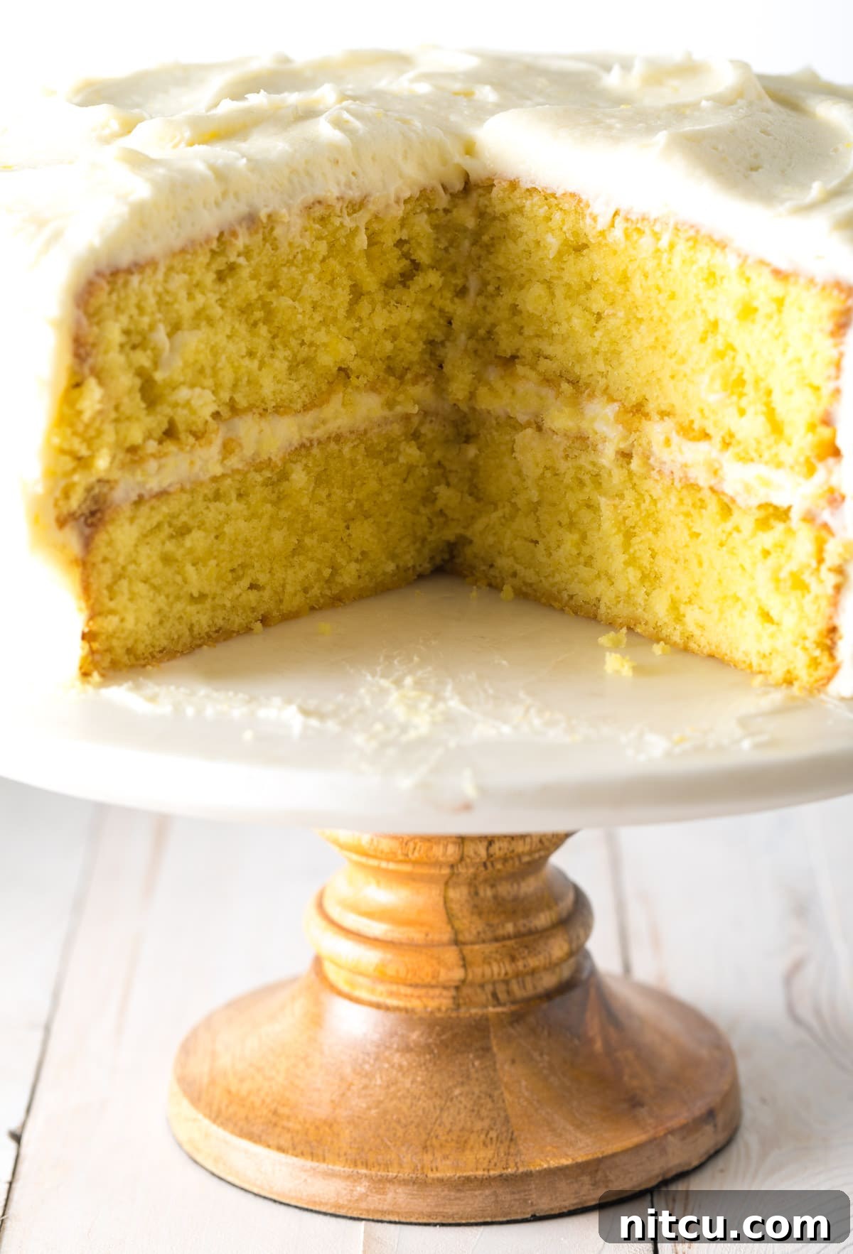 A stunning lemon buttermilk cake elegantly presented on a cake stand, with one perfect slice already removed, showcasing its beautiful layers.