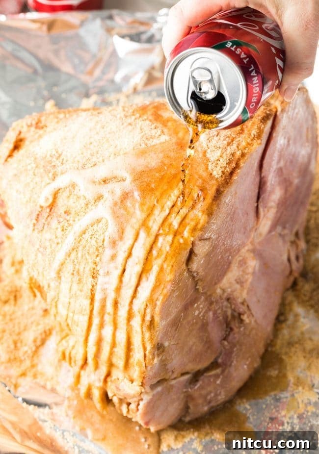 A hand gently pours a can of Coca-Cola over the ham, ensuring it coats all surfaces before the baking process begins.