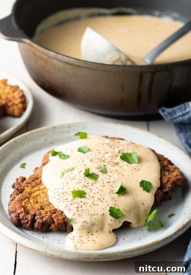 Chicken Fried Steak recipe: A perfectly plated chicken fried steak, generously smothered in white gravy, presented beautifully on a rustic dinner setting.