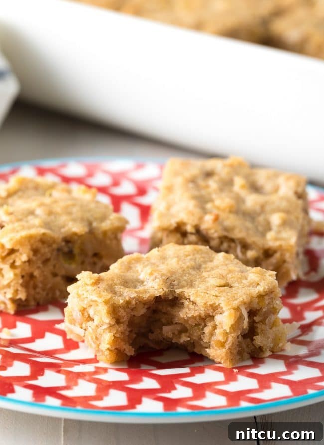 Three golden hummingbird blondies on a plate, with one bar showing a delicious bite taken out.