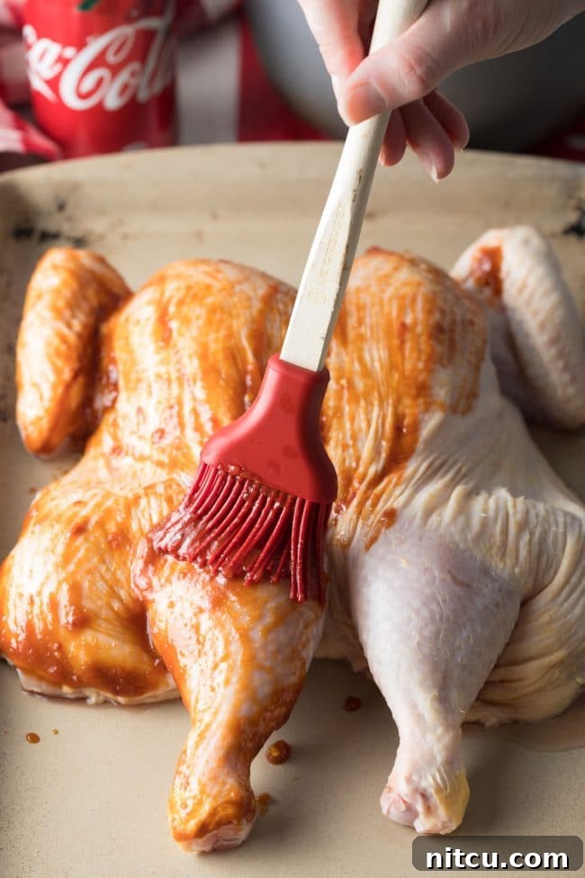 Spreading coca cola sauce across spatchcock chicken before roasting.