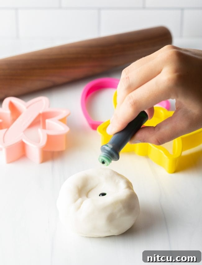 Hand adding food coloring to homemade fondant.