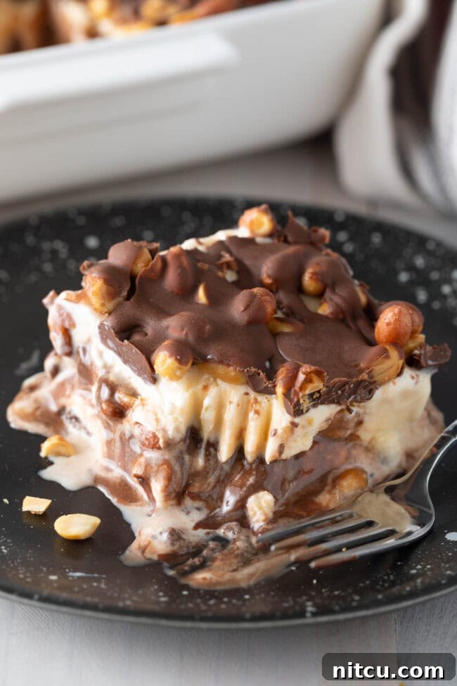 A close-up of a homemade Buster Bar Ice Cream Cake slice on a plate, with a portion bitten off.
