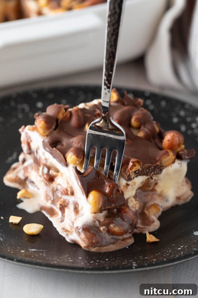 A tempting piece of Buster Bar Ice Cream Cake with a fork taking a bite, showcasing the layers.