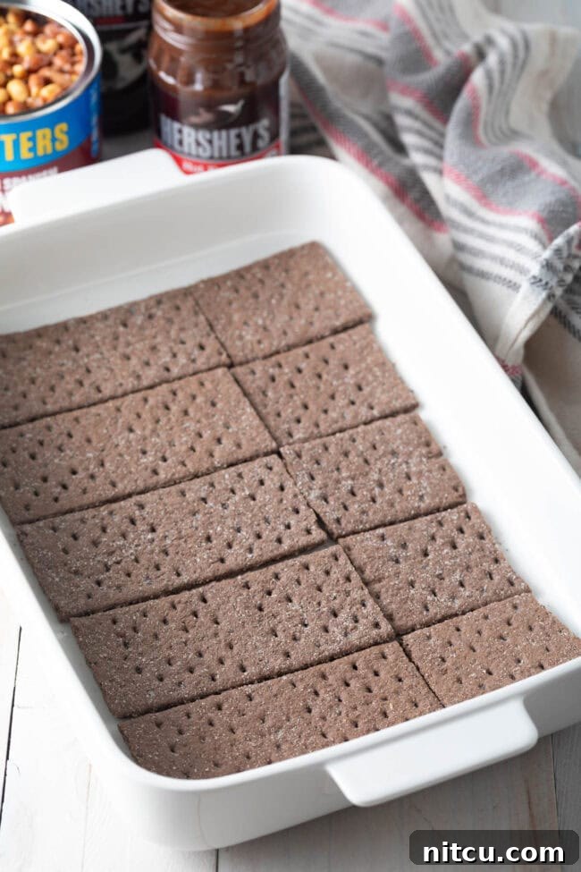 First layer of chocolate graham crackers meticulously arranged in a white baking dish.