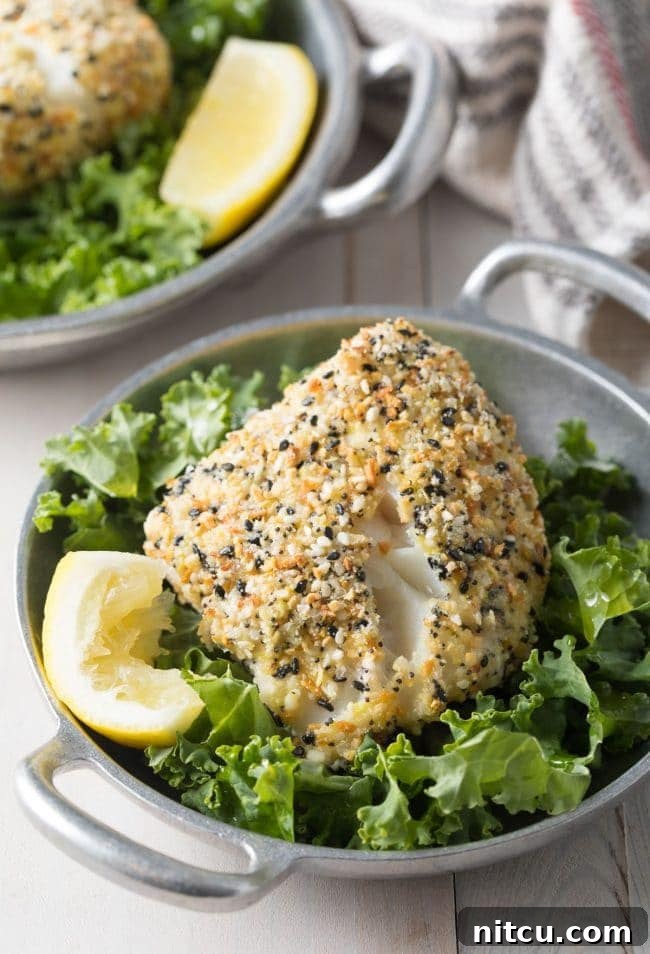 Baked White Fish with Everything Bagel Crust served on a bed of lettuce with a lemon wedge. 