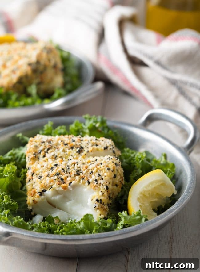 Cod with an everything bagel seasoning crust with some of it flaked off to show the inside of the fish. 