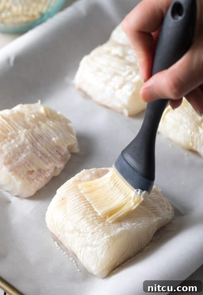 Hand using a brush to brush the fish with mayonnaise to help the seasoning bind to the fish. 