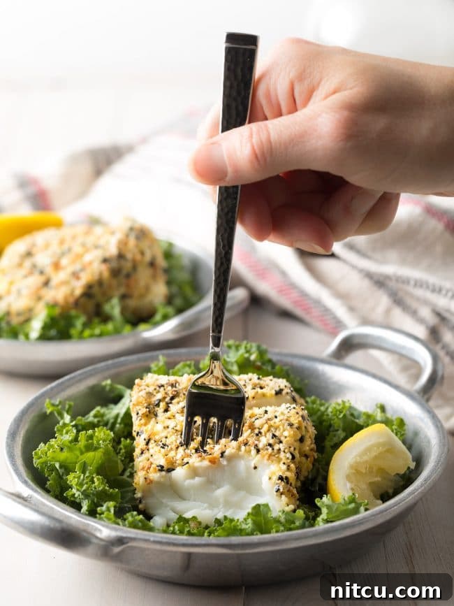 Hand using a fork to flake off a piece of fish from the cod. 