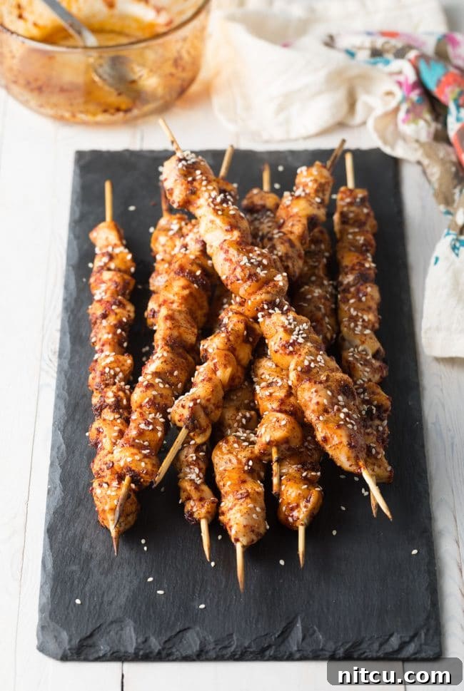 A plate of freshly grilled Korean chicken skewers, garnished with sesame seeds.