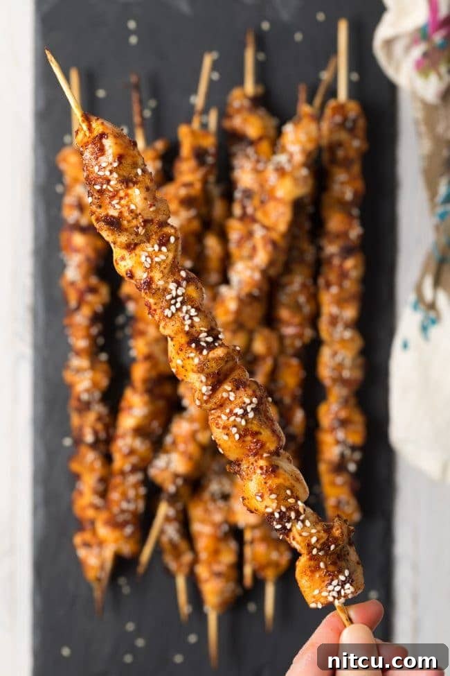 Three Korean chicken skewers resting on a wooden board with fresh herbs.