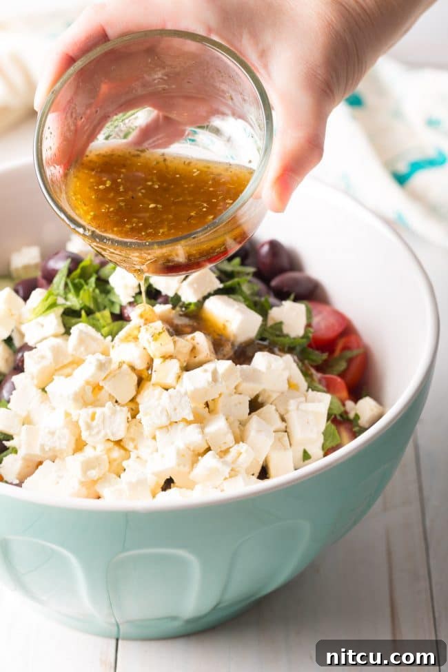 Best Greek Horiatiki (Village Salad) Recipe showing the dressing being poured over the salad. #greek #salad #glutenfree #lowcarb #keto #vegetarian