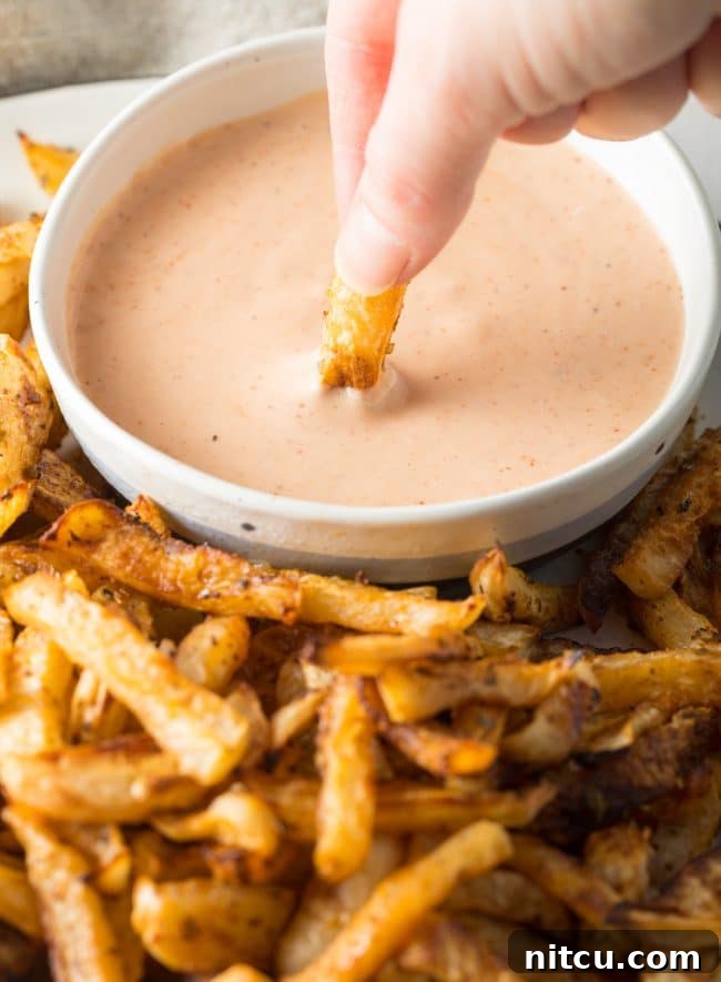 Low Carb Baked Turnip Fries being dipped into a creamy sauce, showcasing their appeal as a healthy alternative.