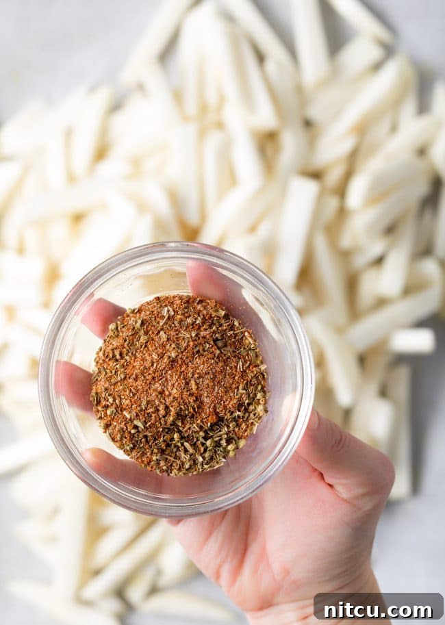 Hand seasoning thinly sliced turnip fries before baking, demonstrating a key step in preparation.