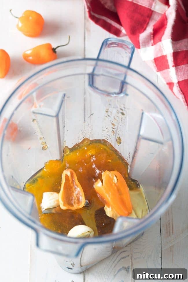 Halved habanero peppers in a blender jar with peach jam and cloves of garlic.